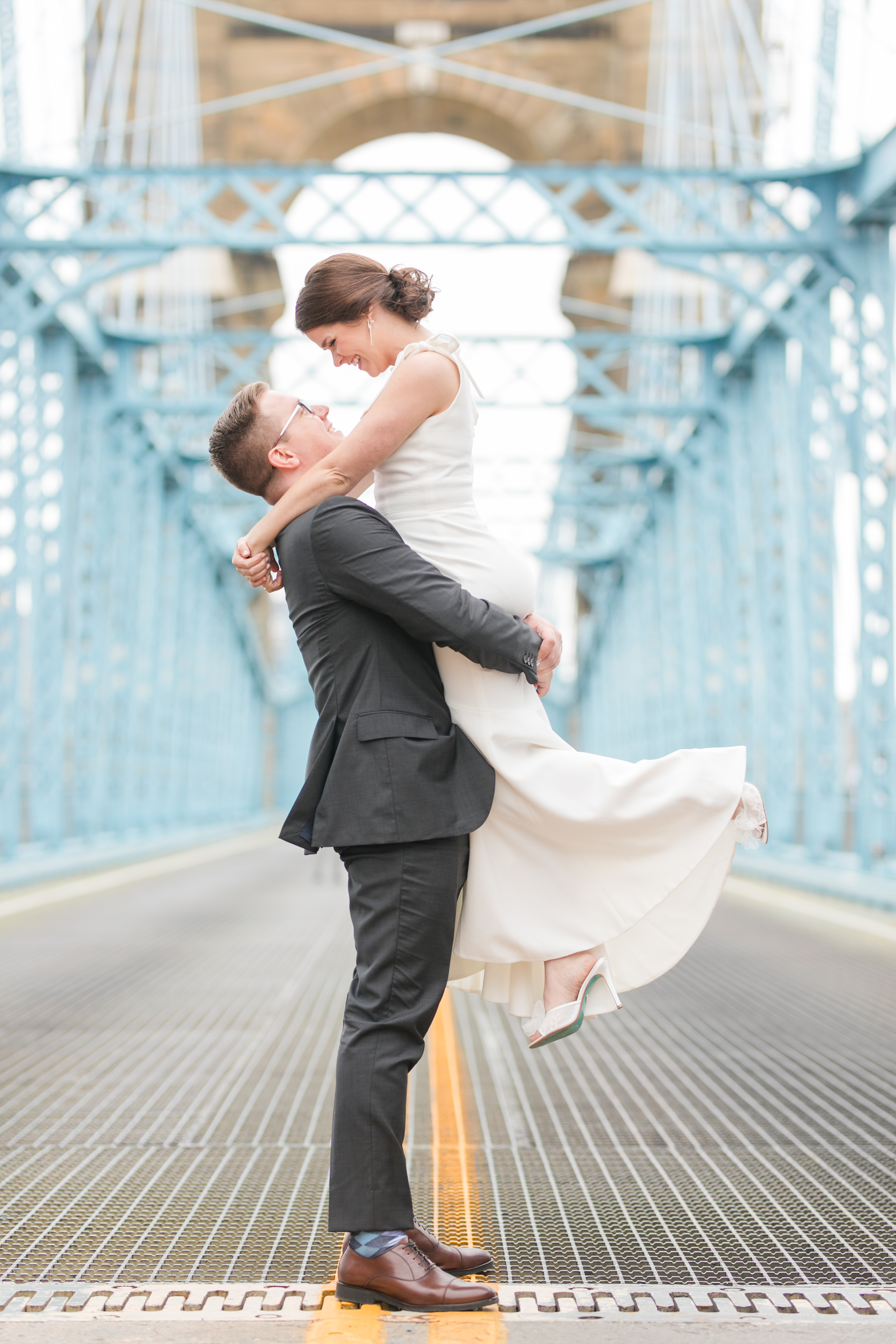 Northern Kentucky Wedding featuring the Roebling Brigde with a groom picking up a bride in a white dress