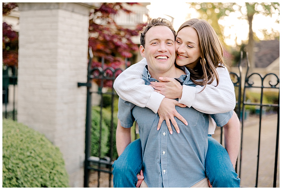 young brunette man holding his fiance on his back. She is laughing.